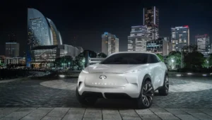 SUV concept de Infiniti en color blanco exhibido de noche frente al skyline iluminado de una ciudad asiática.