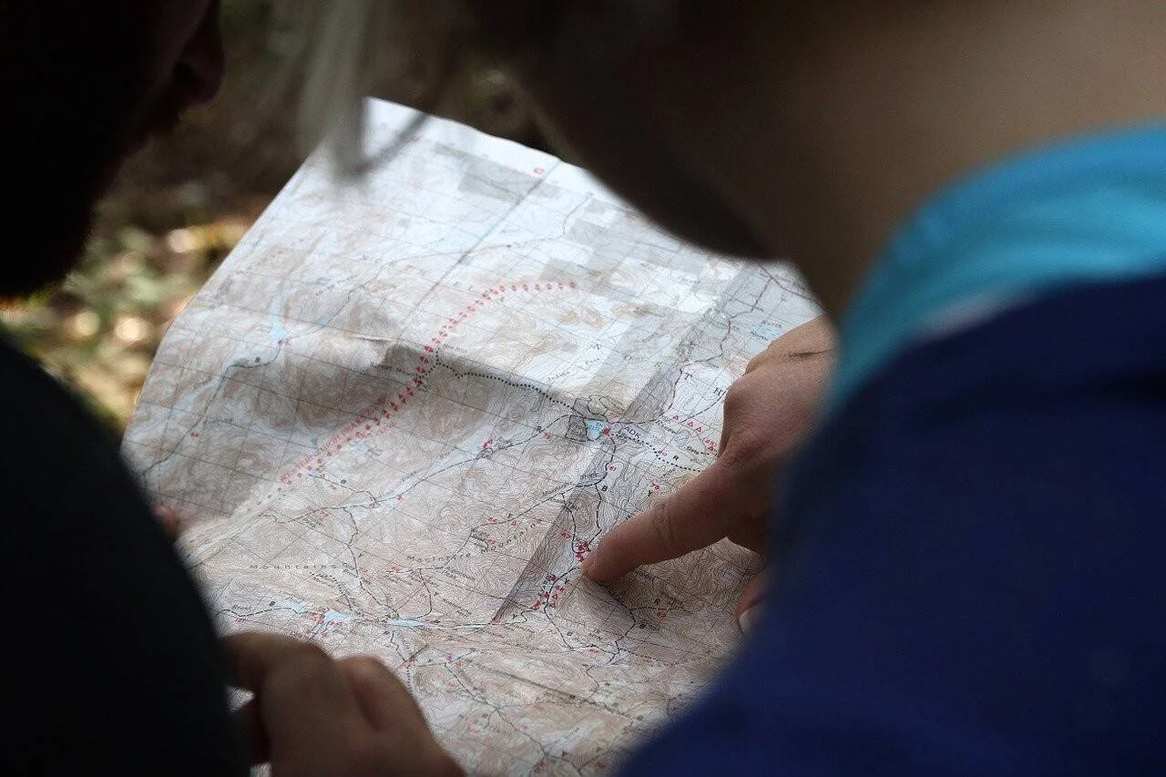Dos personas señalan un punto en un mapa topográfico de papel durante una excursión al aire libre.
