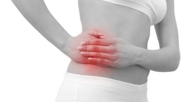 Mujer en blanco y negro sostiene su costado derecho con las manos, con zona roja que indica dolor abdominal lateral.