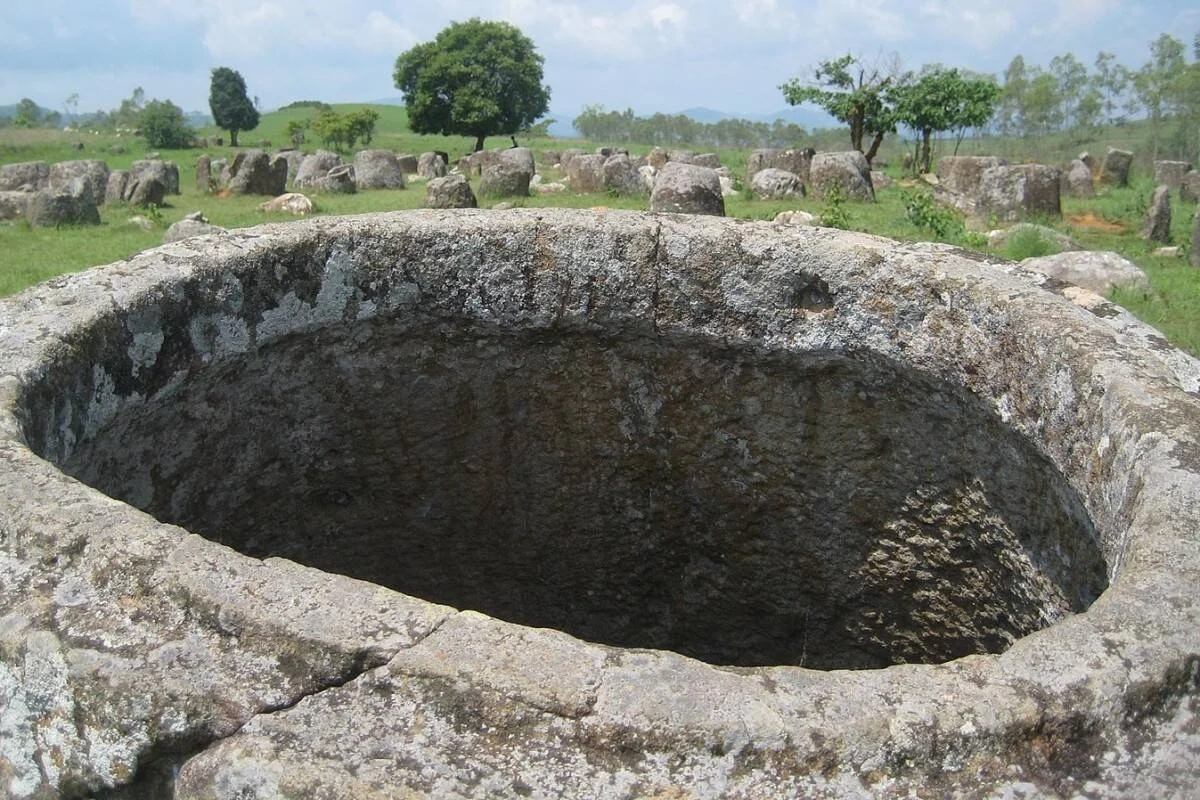 Interior hueco de una gran jarra de piedra prehistórica en la Llanura de las Jarras, Laos, con decenas de jarras dispersas en el campo al fondo.