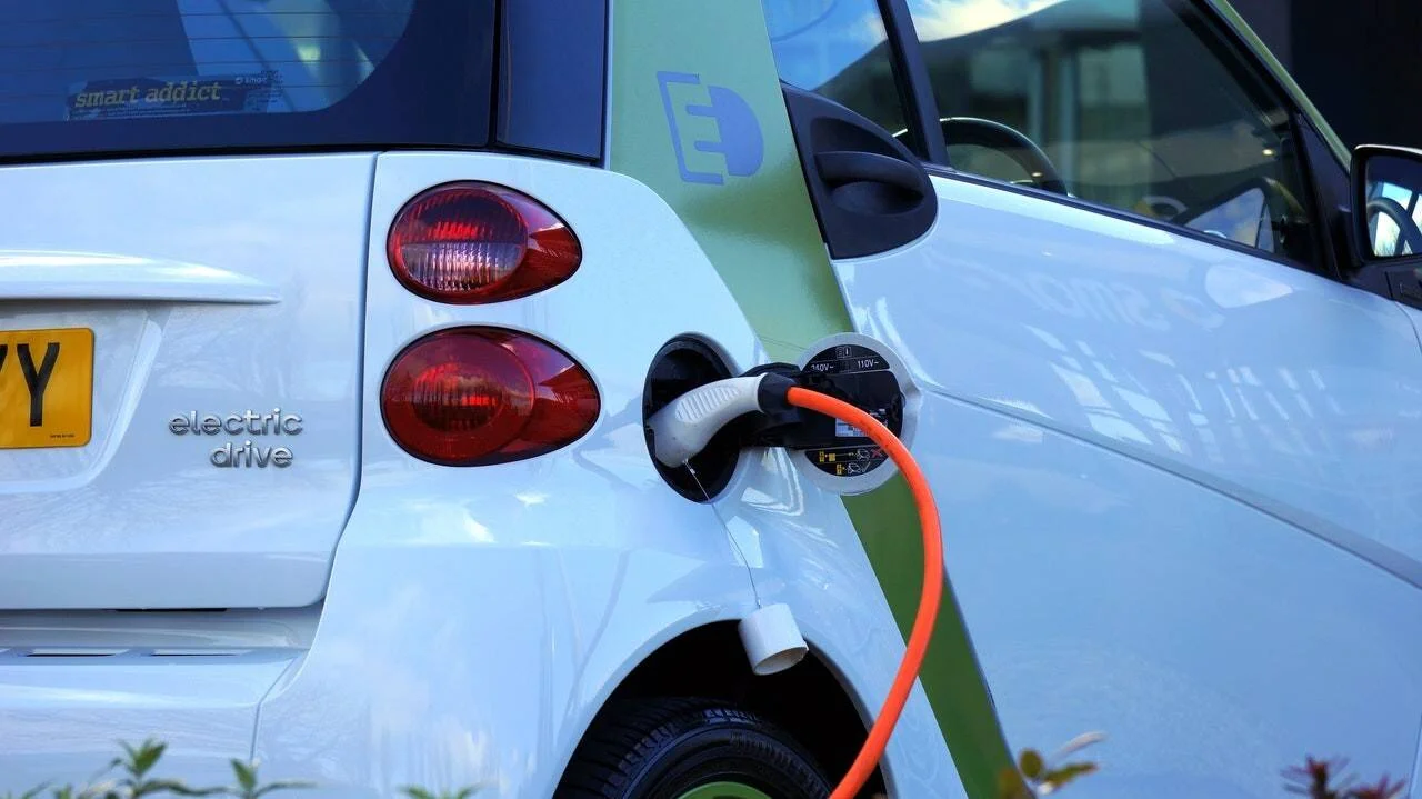 Un Smart Electric Drive blanco se recarga con un cable naranja conectado a su puerto de carga.