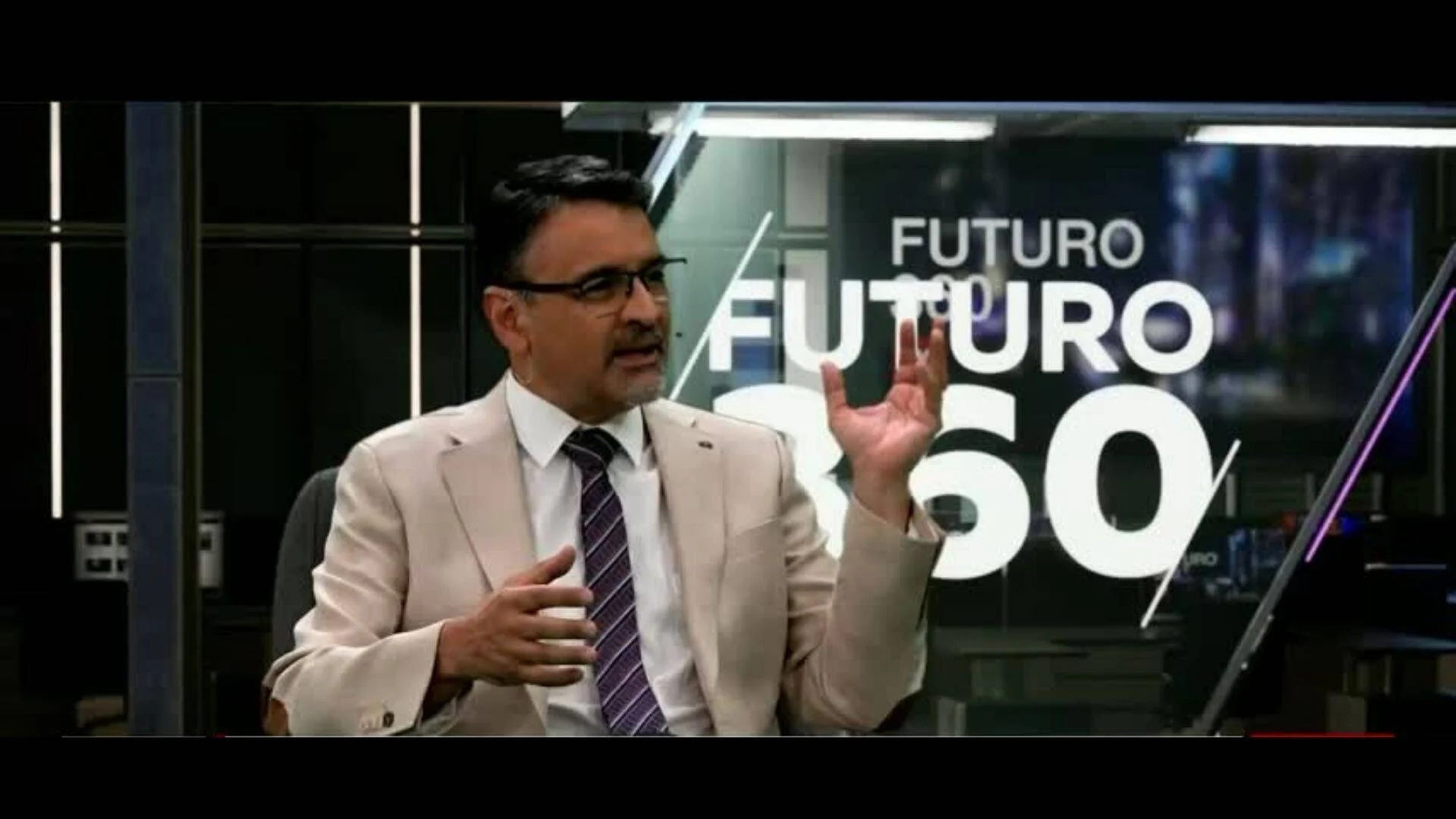 Hombre con traje beige y corbata gesticula mientras habla en el set del programa televisivo Futuro 360.
