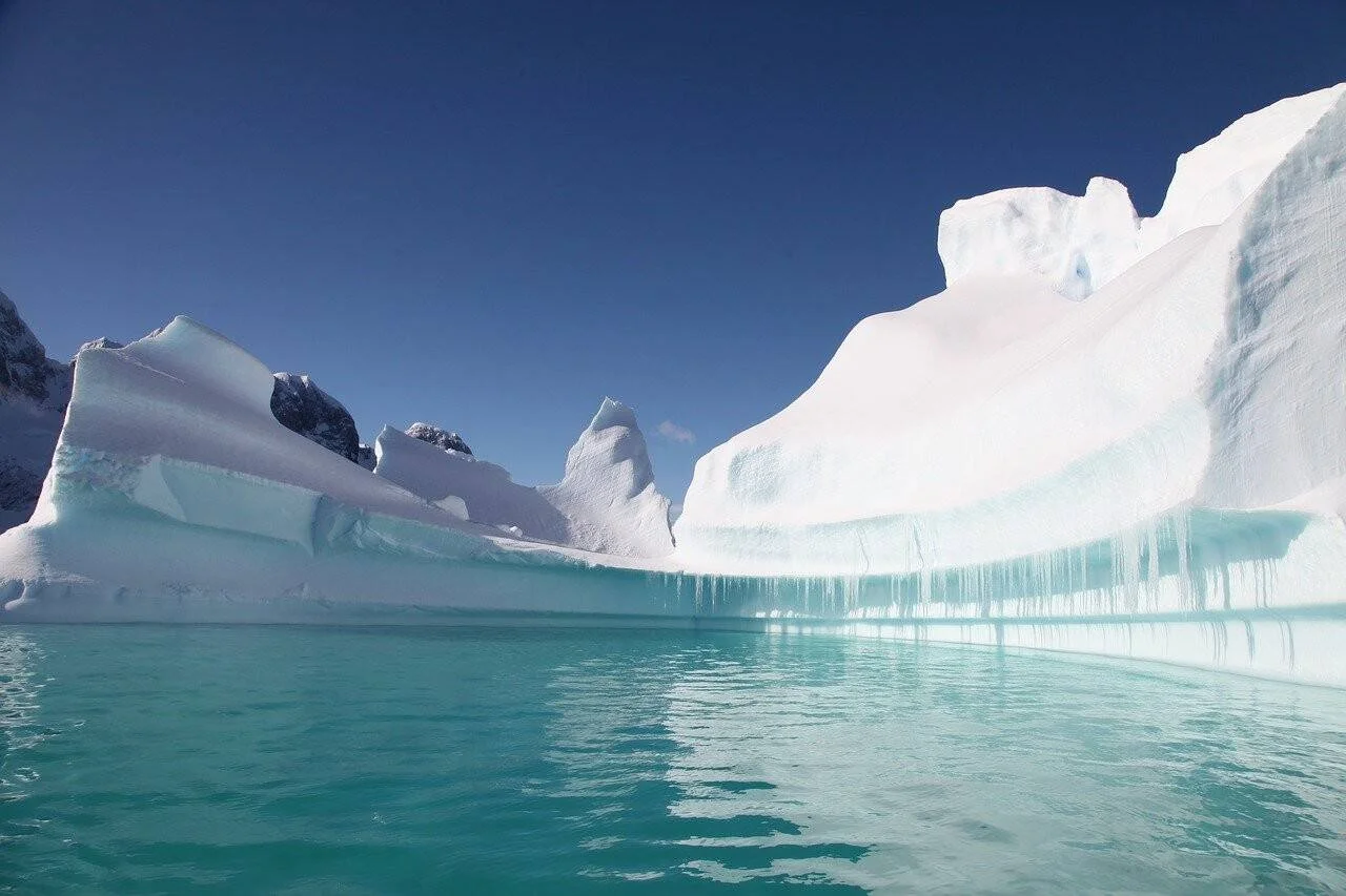 Grandes icebergs blancos con tonos azul verdoso emergen de aguas turquesa bajo un cielo azul despejado en una región polar.