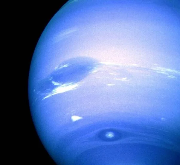 Vista del planeta Neptuno mostrando la Gran Mancha Oscura y nubes blancas en su atmósfera azul.
