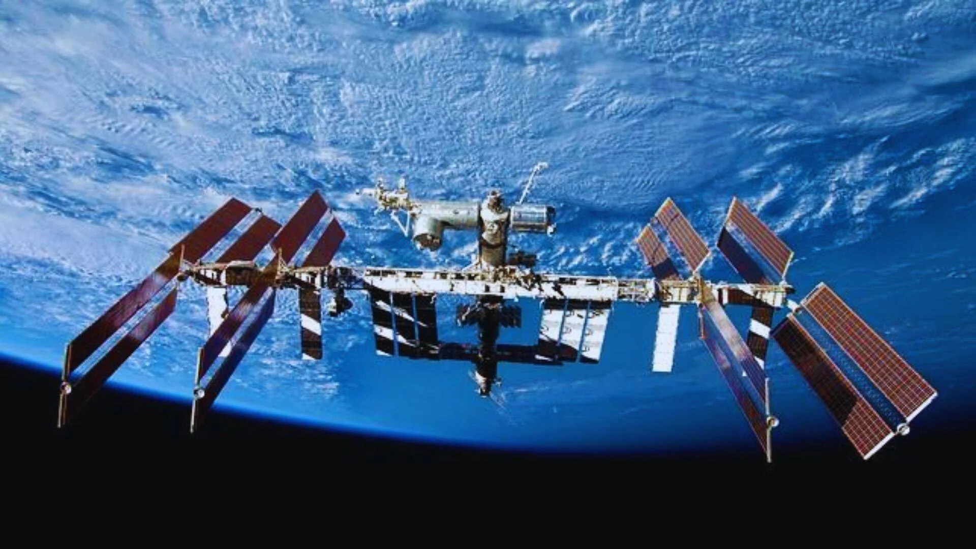 La Estación Espacial Internacional con sus paneles solares desplegados flota en órbita sobre la superficie azul de la Tierra.