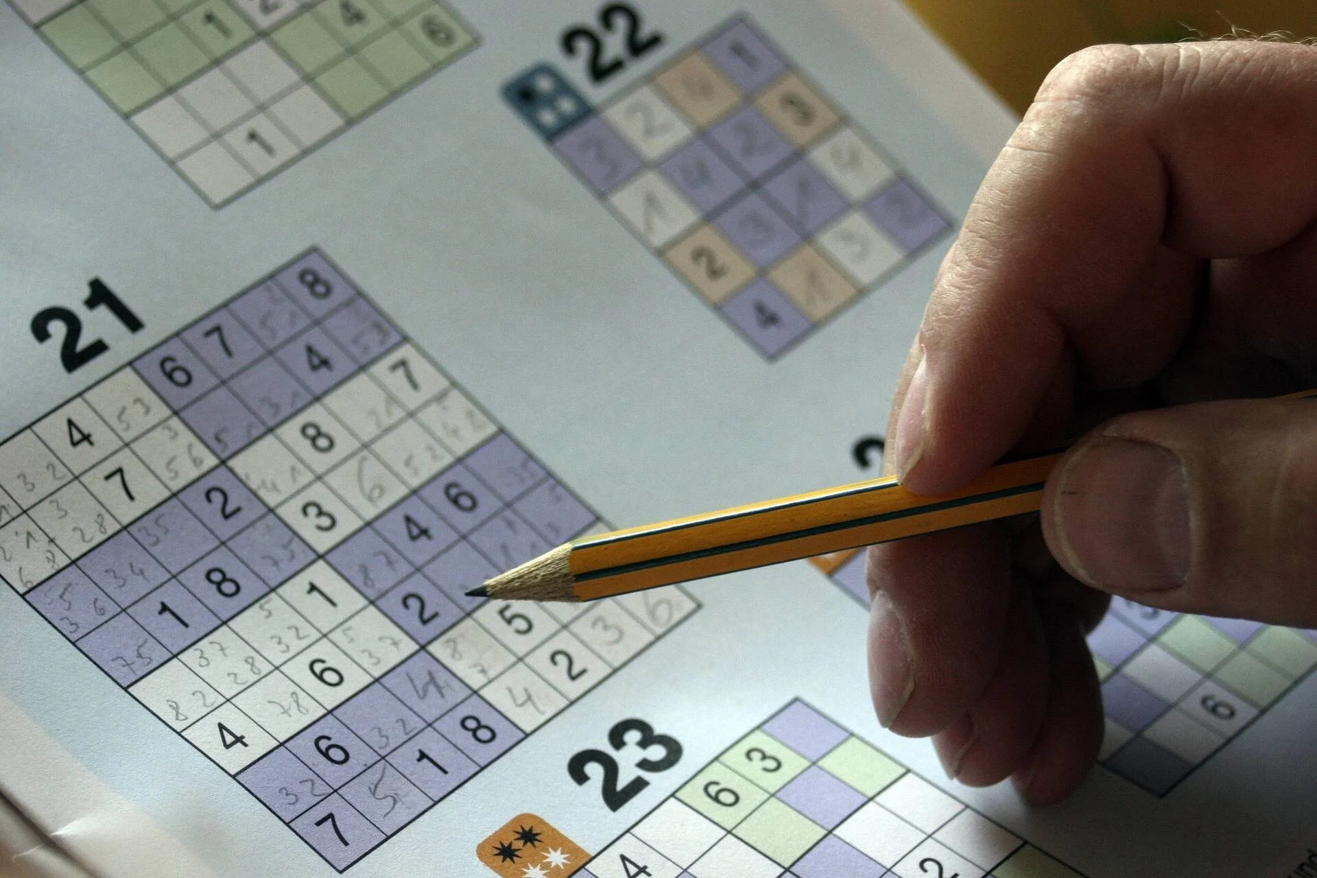Una mano sostiene un lápiz sobre una página con varios puzzles de sudoku parcialmente resueltos.