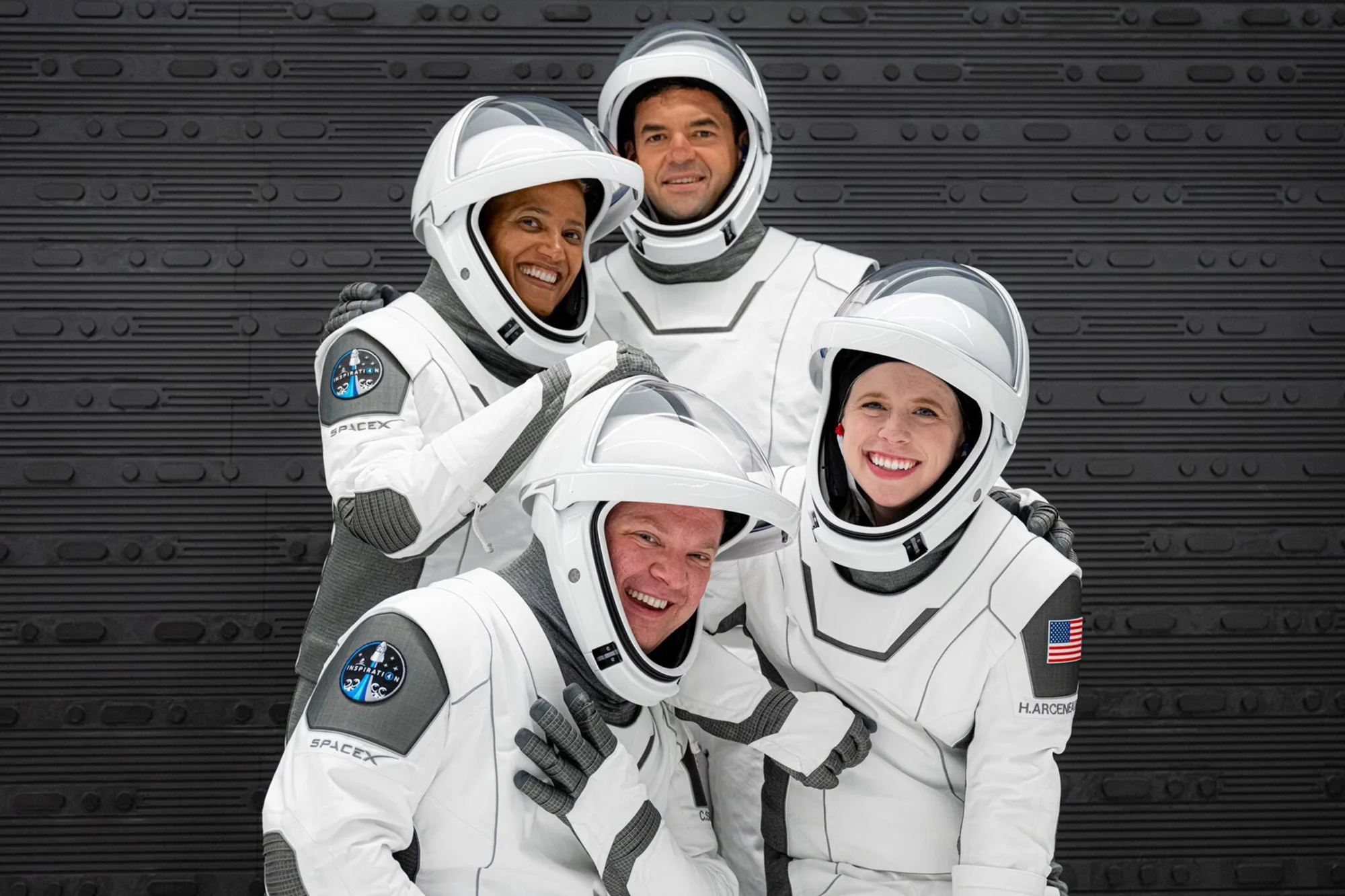 Cuatro personas con trajes espaciales blancos de SpaceX y el parche Inspiration4 posan sonrientes para una foto grupal.