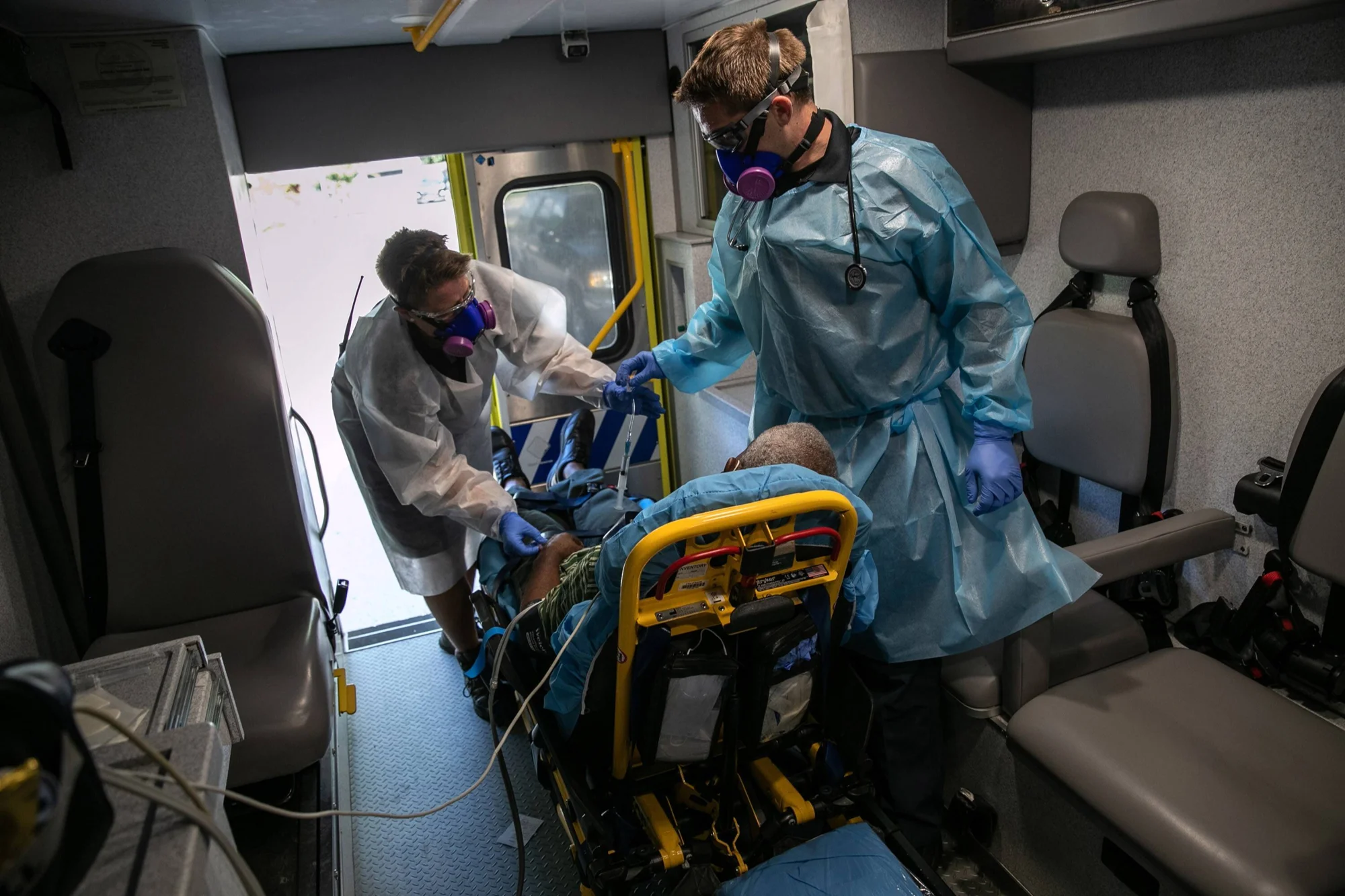 Dos paramédicos con equipo de protección personal atienden a un paciente sobre una camilla dentro de una ambulancia.