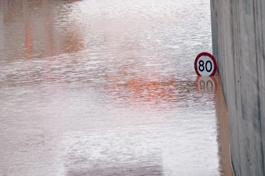 Carretera completamente inundada con agua turbia que cubre casi por completo una señal de límite de velocidad de 80 km/h.