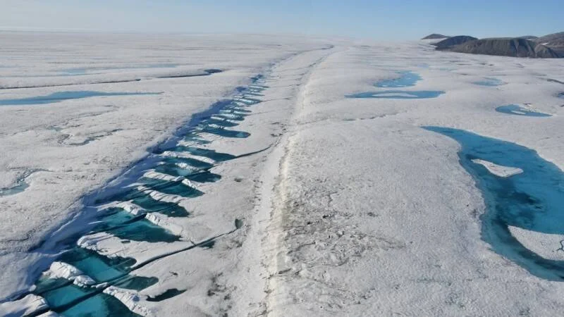 Vista aérea de un glaciar con grietas y pozas de agua de deshielo de color azul turquesa en su superficie.