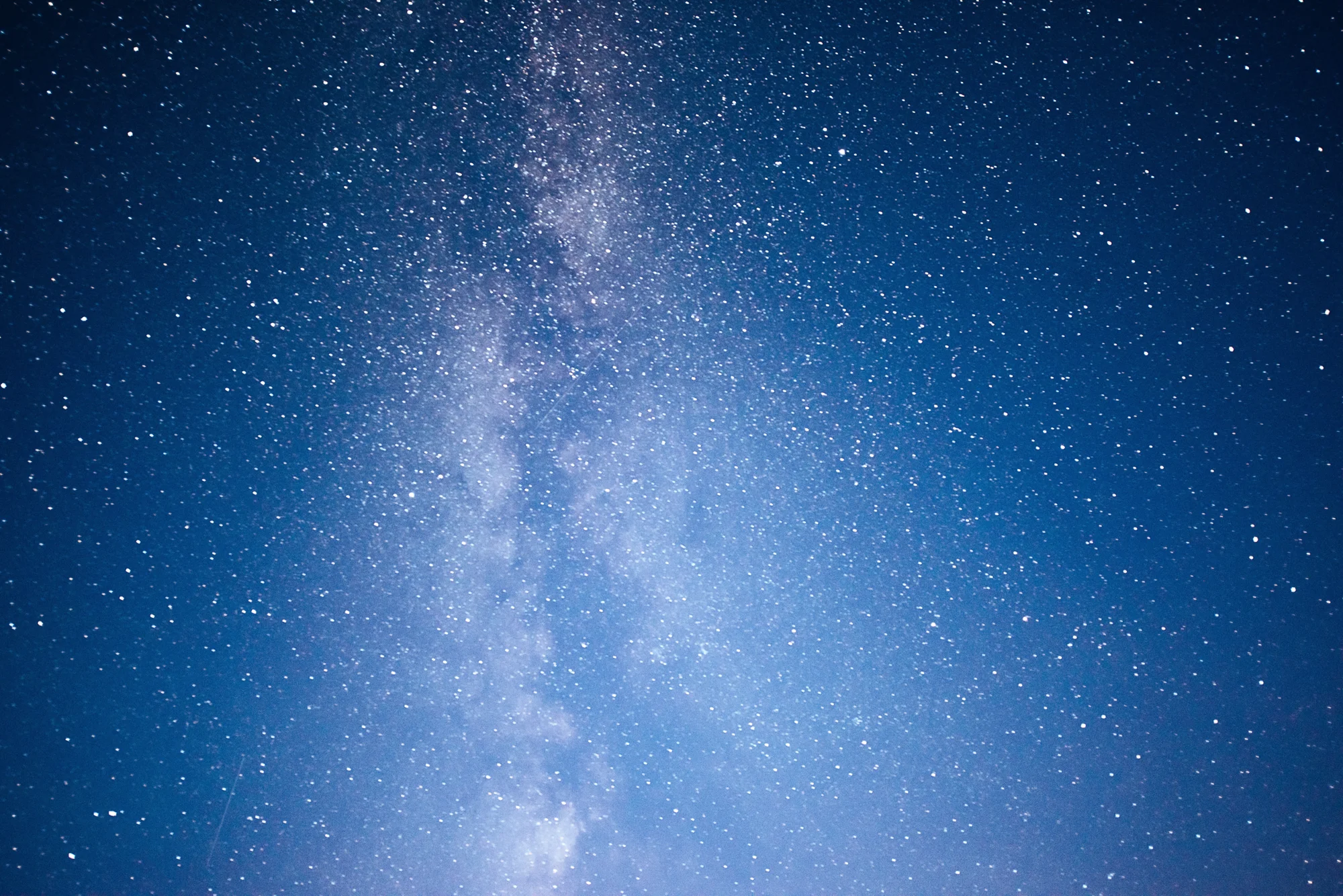 La Vía Láctea se extiende verticalmente en un cielo nocturno azul profundo repleto de estrellas.