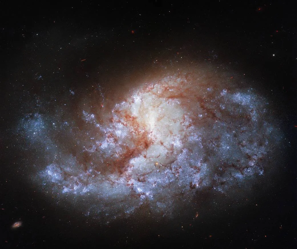 Galaxia espiral con núcleo luminoso dorado, brazos azules de formación estelar y filamentos rojizos de polvo interestelar sobre fondo negro.