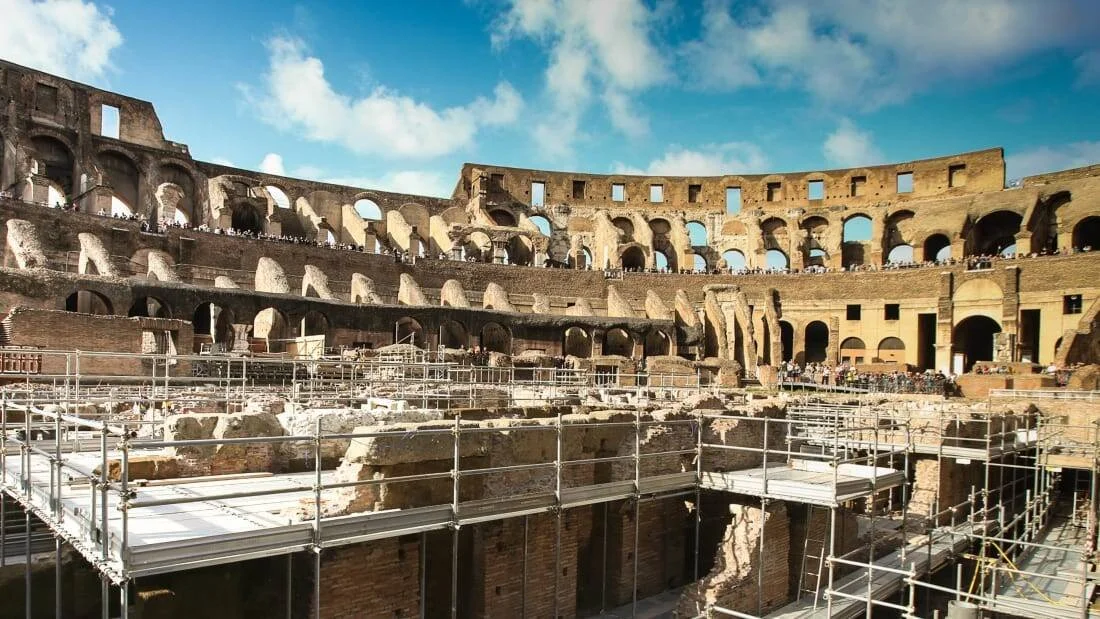 Vista interior del Coliseo de Roma con andamios metálicos sobre la arena en obras de restauración y visitantes en las gradas.