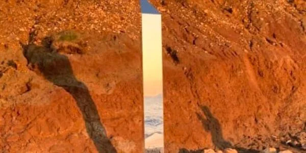 Columna metálica brillante vertical encajada entre rocas de color rojizo en un paisaje árido.