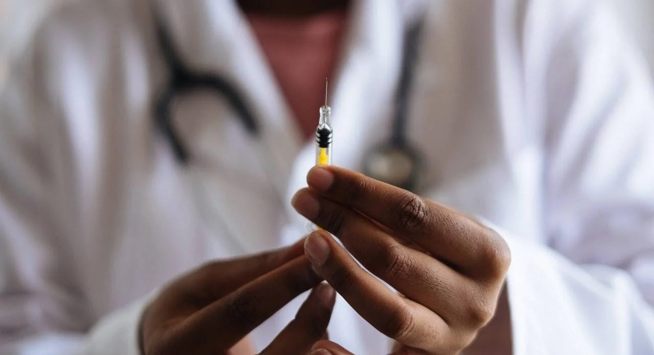 Profesional de salud con guardapolvo y estetoscopio sostiene una jeringa lista para aplicar una inyección.