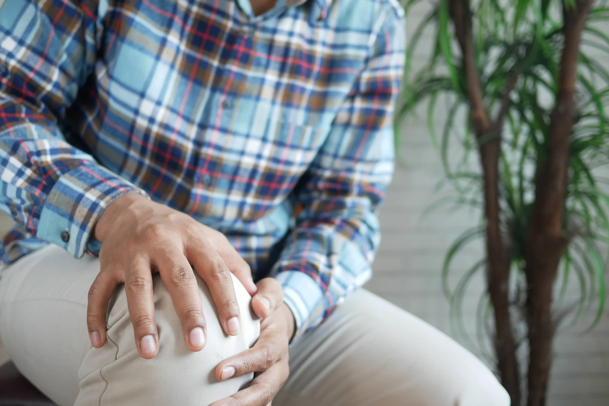 Persona con camisa a cuadros sujeta su rodilla con ambas manos, gesto que indica dolor articular.