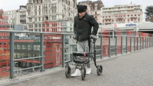 Hombre joven con andador de ruedas camina por un puente urbano cerca de una estación de metro en Lausana, Suiza.