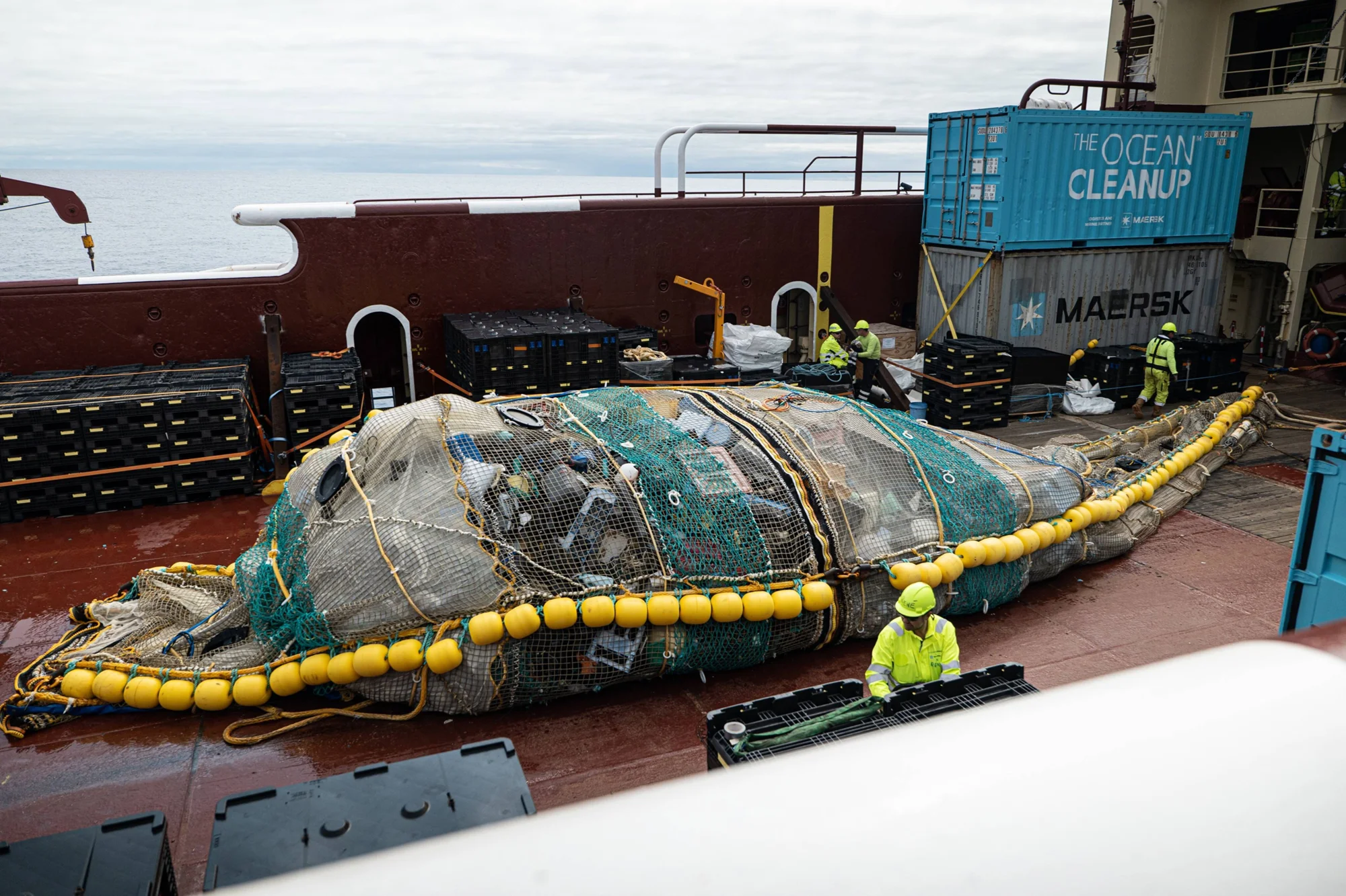 Trabajadores de The Ocean Cleanup manipulan una enorme red llena de plásticos y residuos marinos sobre la cubierta de un barco en alta mar.