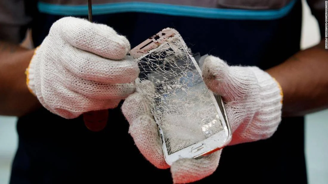 Manos con guantes blancos sostienen un teléfono móvil con la pantalla completamente agrietada durante su desmantelamiento.