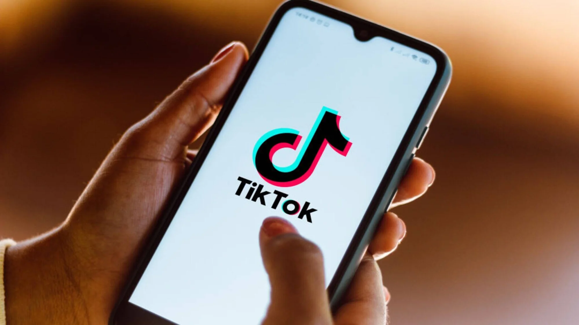 Una mano sostiene un smartphone que muestra el logo y nombre de la app TikTok en pantalla.