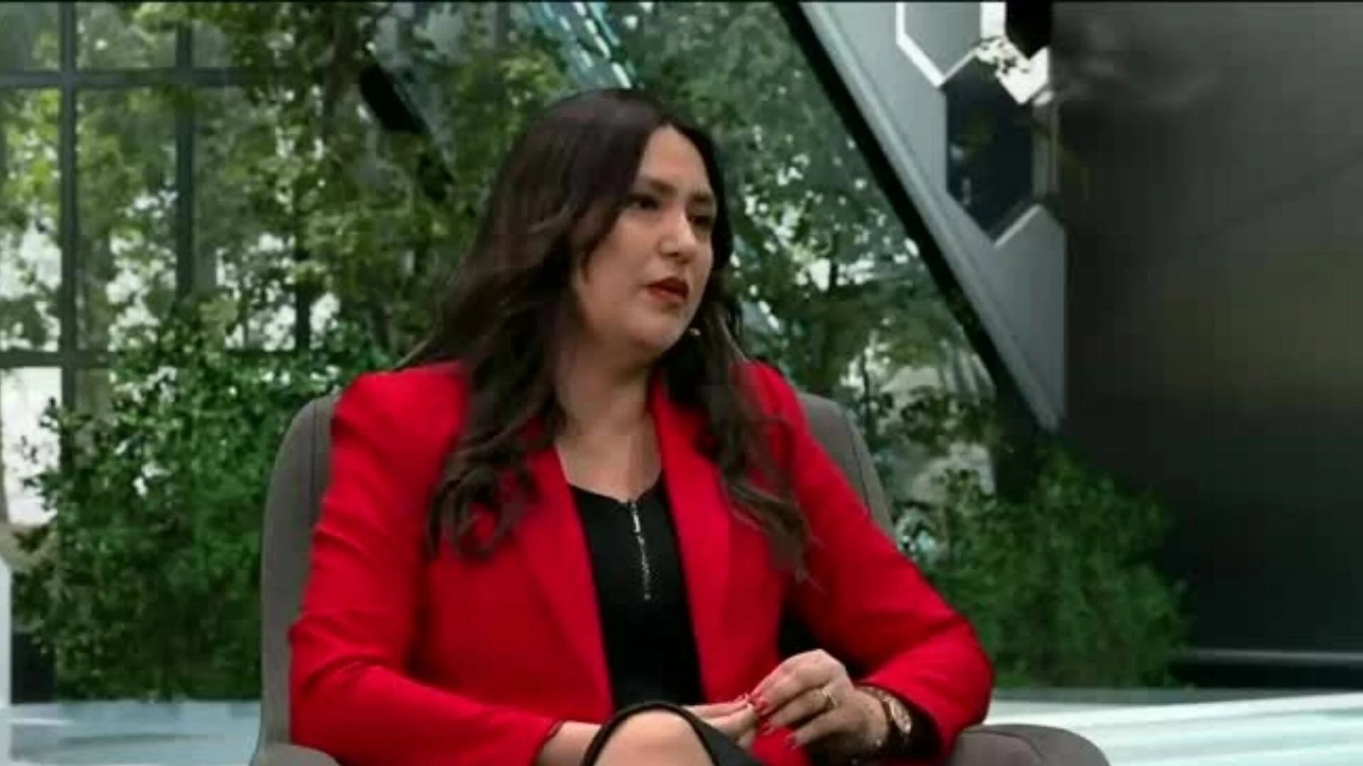 Mujer de cabello oscuro con saco rojo sentada en un estudio de televisión durante una entrevista.