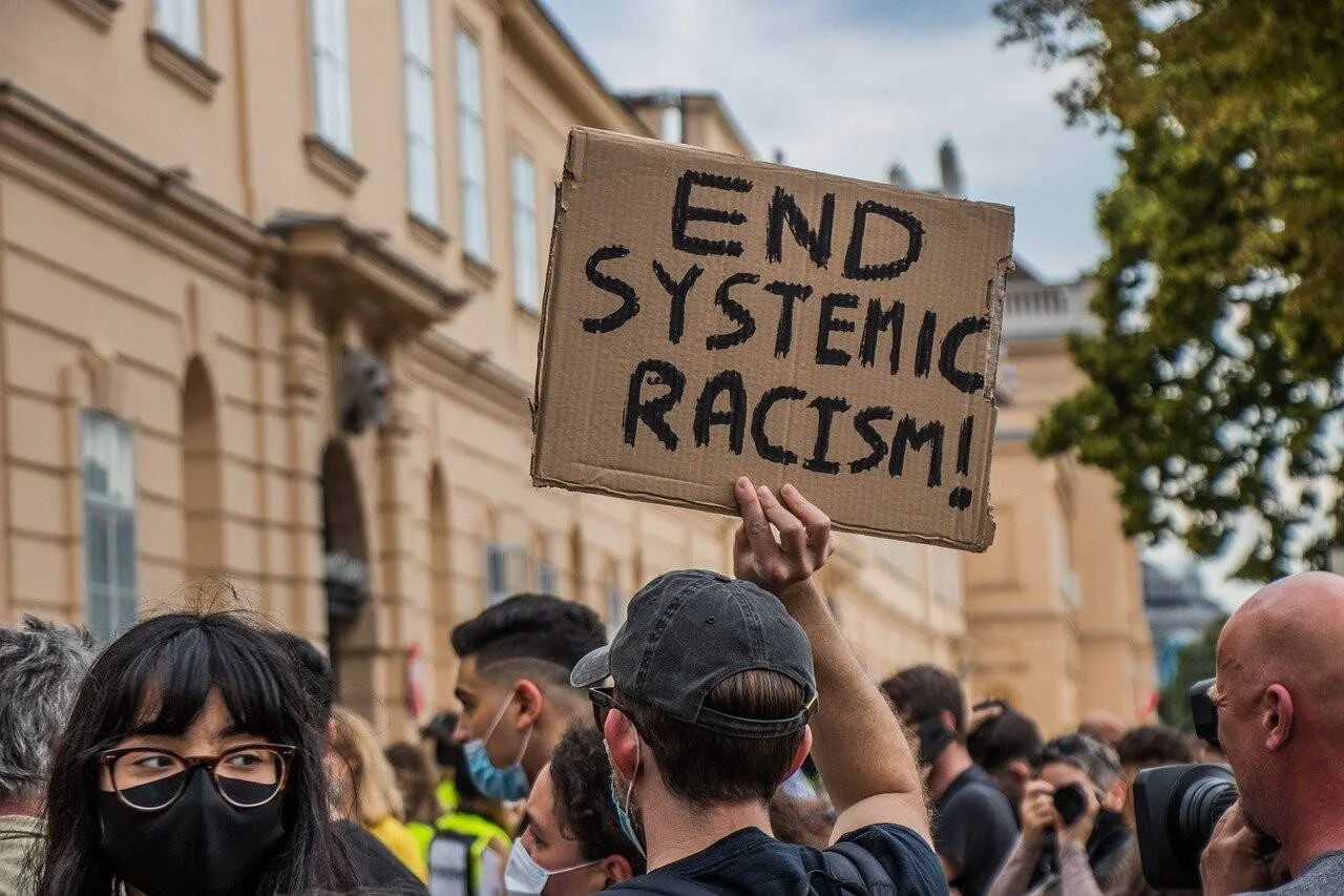 Un manifestante levanta un cartel de cartón con el mensaje 'End Systemic Racism!' en una multitudinaria protesta callejera.