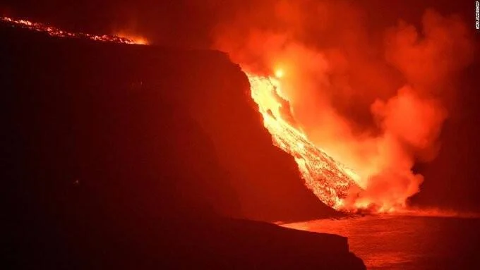 Torrente de lava incandescente desciende por un acantilado y llega al océano generando grandes nubes de vapor.