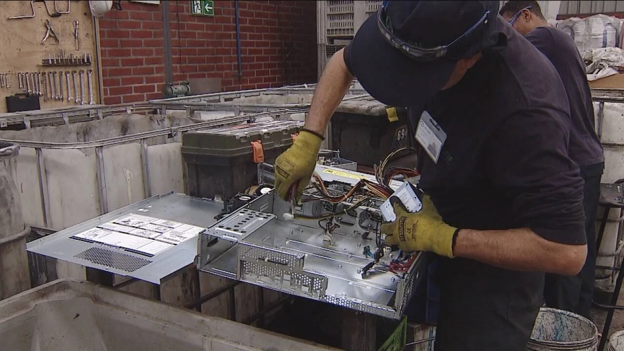 Operario con guantes desensambla componentes de una computadora en un taller de reciclaje de residuos electrónicos.