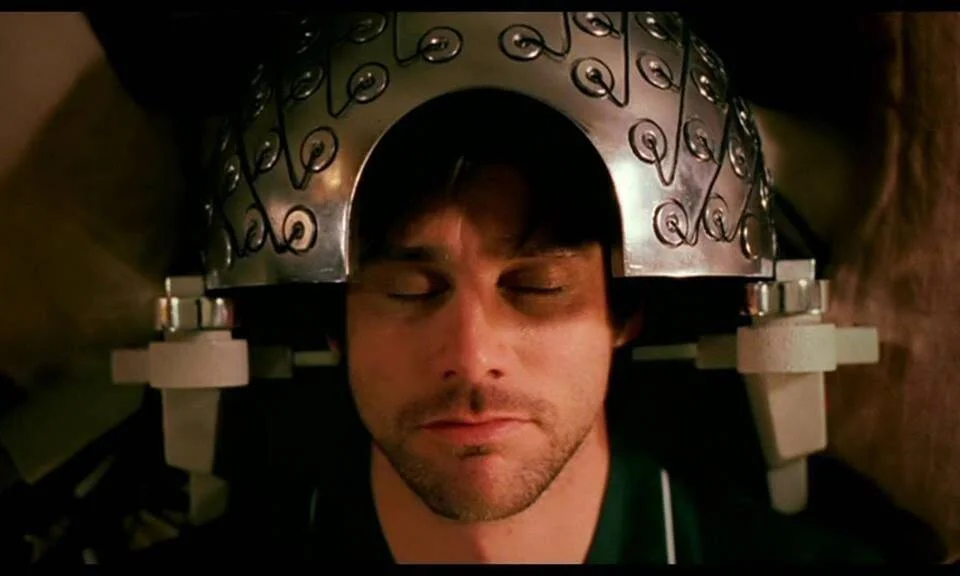 Un hombre con los ojos cerrados lleva un elaborado casco metálico con electrodos, en una escena de película de ciencia ficción.