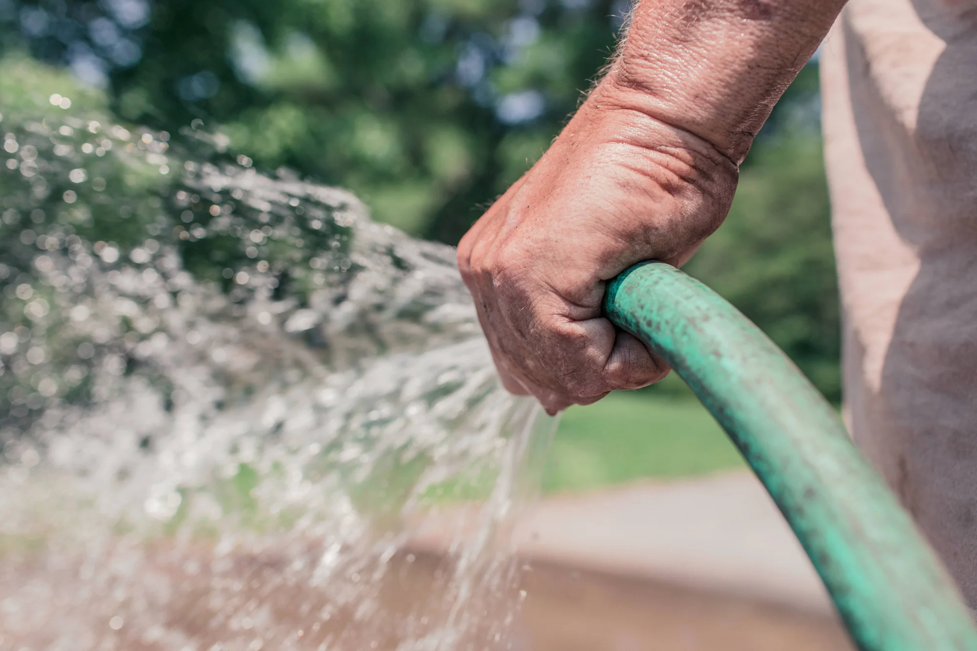 Una mano aprieta una manguera de jardín verde dejando salir un chorro de agua al exterior.