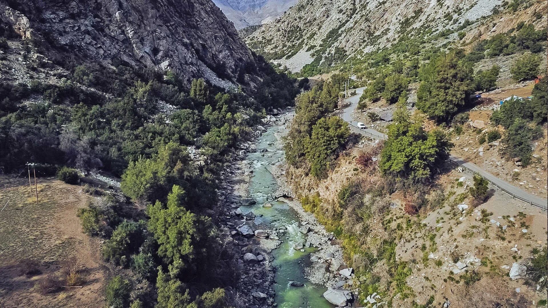 Vista aérea de un río de aguas turquesas fluyendo entre rocas en un cañón montañoso, con una carretera sinuosa y vegetación a los lados.