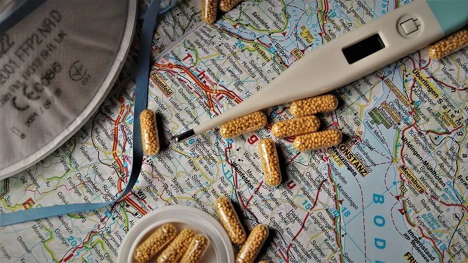 Cápsulas medicinales, termómetro digital y mascarilla FFP2 dispersos sobre un mapa de carreteras, evocando salud en viajes.