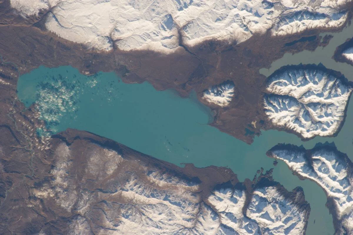 Vista aérea de un lago de aguas turquesas rodeado de montañas cubiertas de nieve y glaciares en la Patagonia.