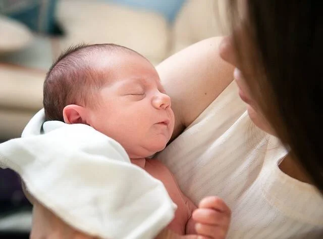 Bebé recién nacido durmiendo plácidamente en brazos de una mujer, envuelto en una tela blanca.