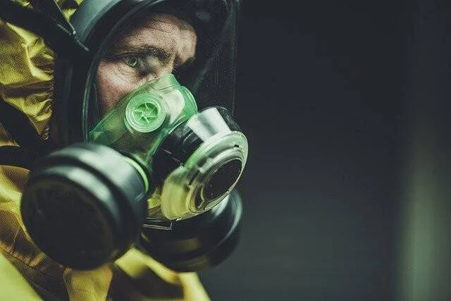 Trabajador con traje de protección química amarillo y máscara antigás de doble filtro mirando hacia la cámara.