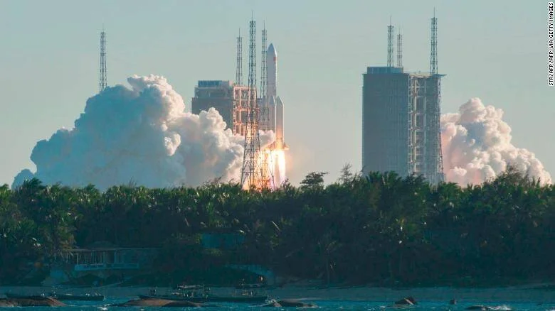 Un cohete despega generando grandes nubes de humo blanco desde una plataforma de lanzamiento costera rodeada de vegetación tropical.