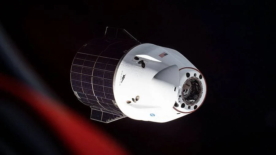 Cápsula espacial Crew Dragon de SpaceX con paneles solares desplegados, flotando en el espacio con fondo negro.