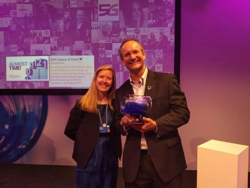 Dos personas sonríen en un escenario mientras sostienen un trofeo azul en el evento The Circulars 2019 en Davos.