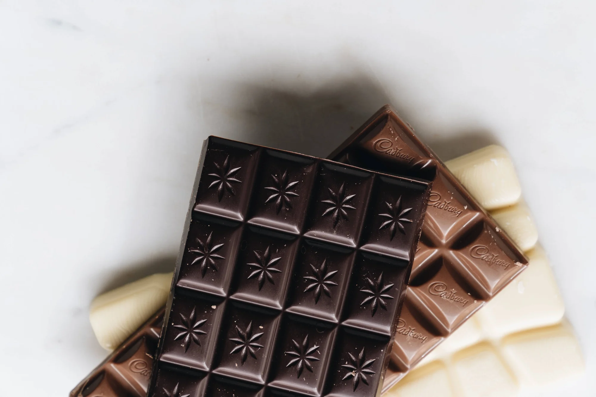 Tabletas de chocolate negro, con leche y blanco apiladas sobre superficie de mármol blanco.