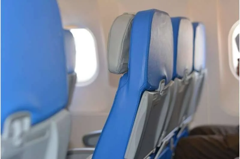 Fila de asientos azules en clase turista de un avión comercial con ventanillas iluminadas al fondo.