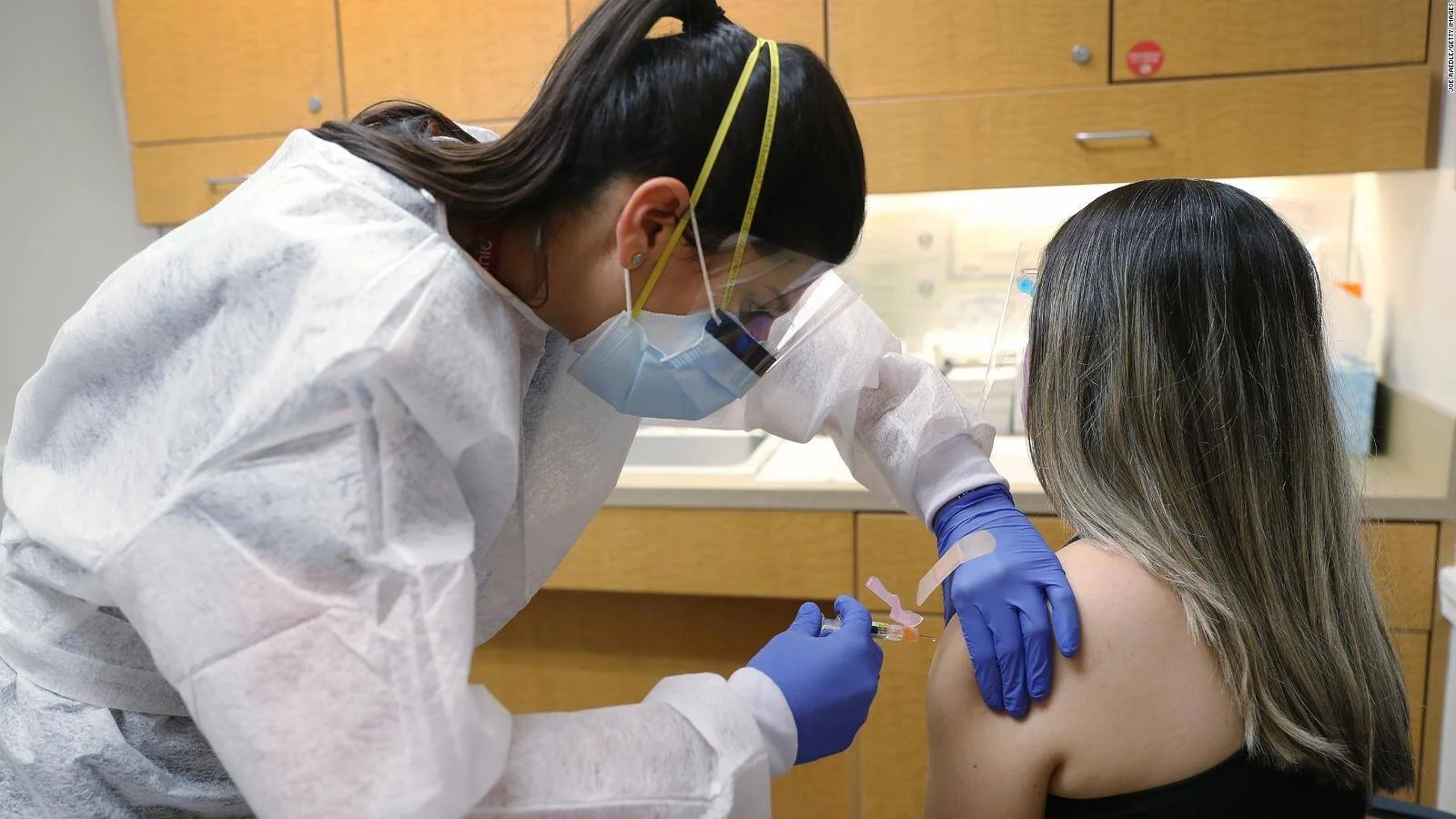 Profesional de salud con mascarilla y guantes aplica una inyección en el brazo de una paciente en un centro médico.