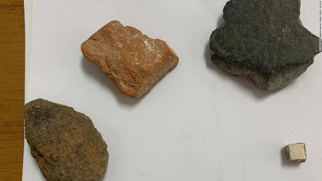 Cuatro fragmentos de piedra y un pequeño trozo de cerámica blanca dispuestos sobre papel, artefactos robados devueltos al Parque Arqueológico de Pompeya.