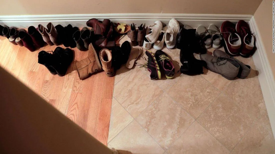 Numerosos pares de zapatos y botas de distintos estilos alineados junto a la pared en la entrada de una vivienda.