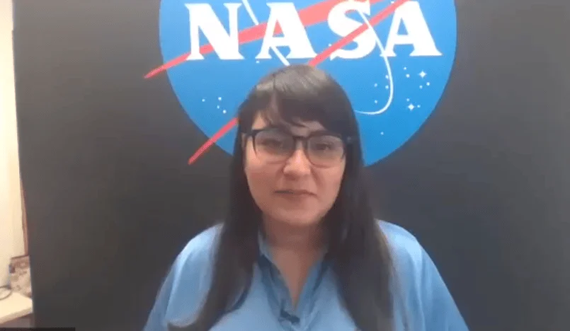 Mujer con camisa azul y anteojos frente al logotipo oficial de la NASA.