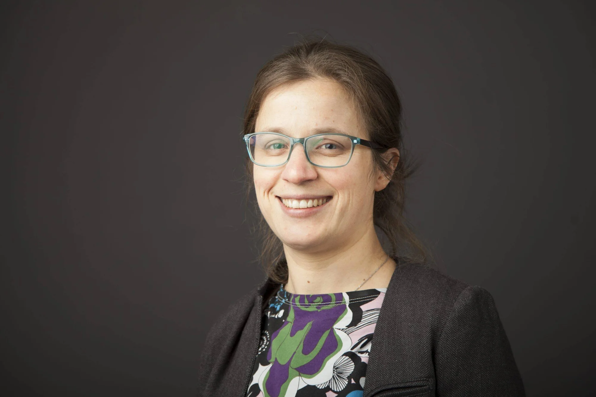 Mujer sonriente con gafas de montura azul y blazer oscuro en foto de perfil profesional.
