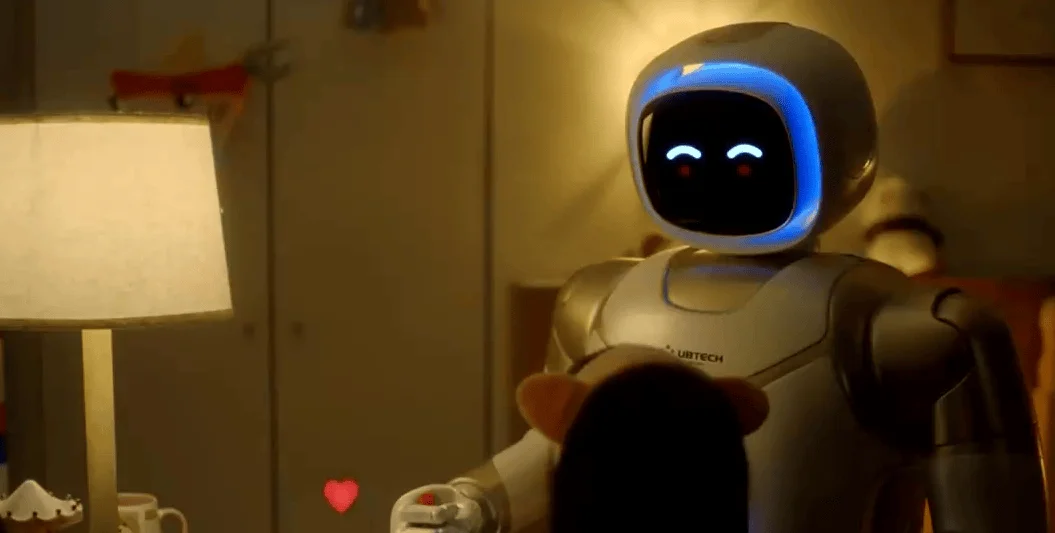 Robot humanoide de UBTECH con cabeza iluminada en azul y ojos LED interactúa con una persona en un entorno hogareño.