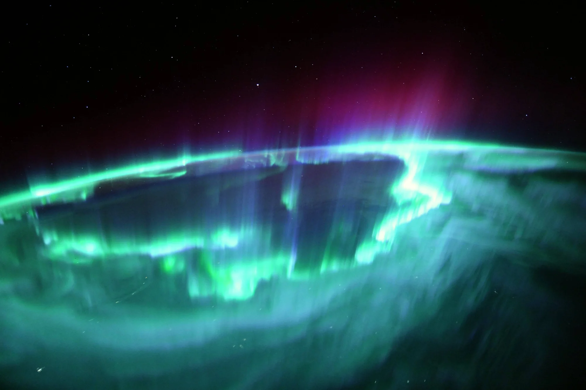 Aurora boreal con cortinas de luz verde, azul y magenta envolviendo la curvatura de la Tierra, fotografiada desde órbita.
