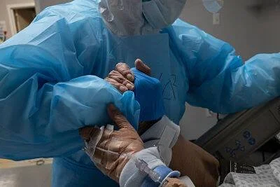 Profesional de salud con equipo de protección toma la mano de un paciente en una cama de hospital.
