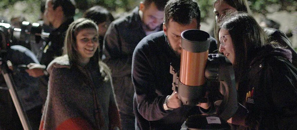 Varias personas se turnan para mirar a través de un telescopio durante una sesión de observación astronómica nocturna.
