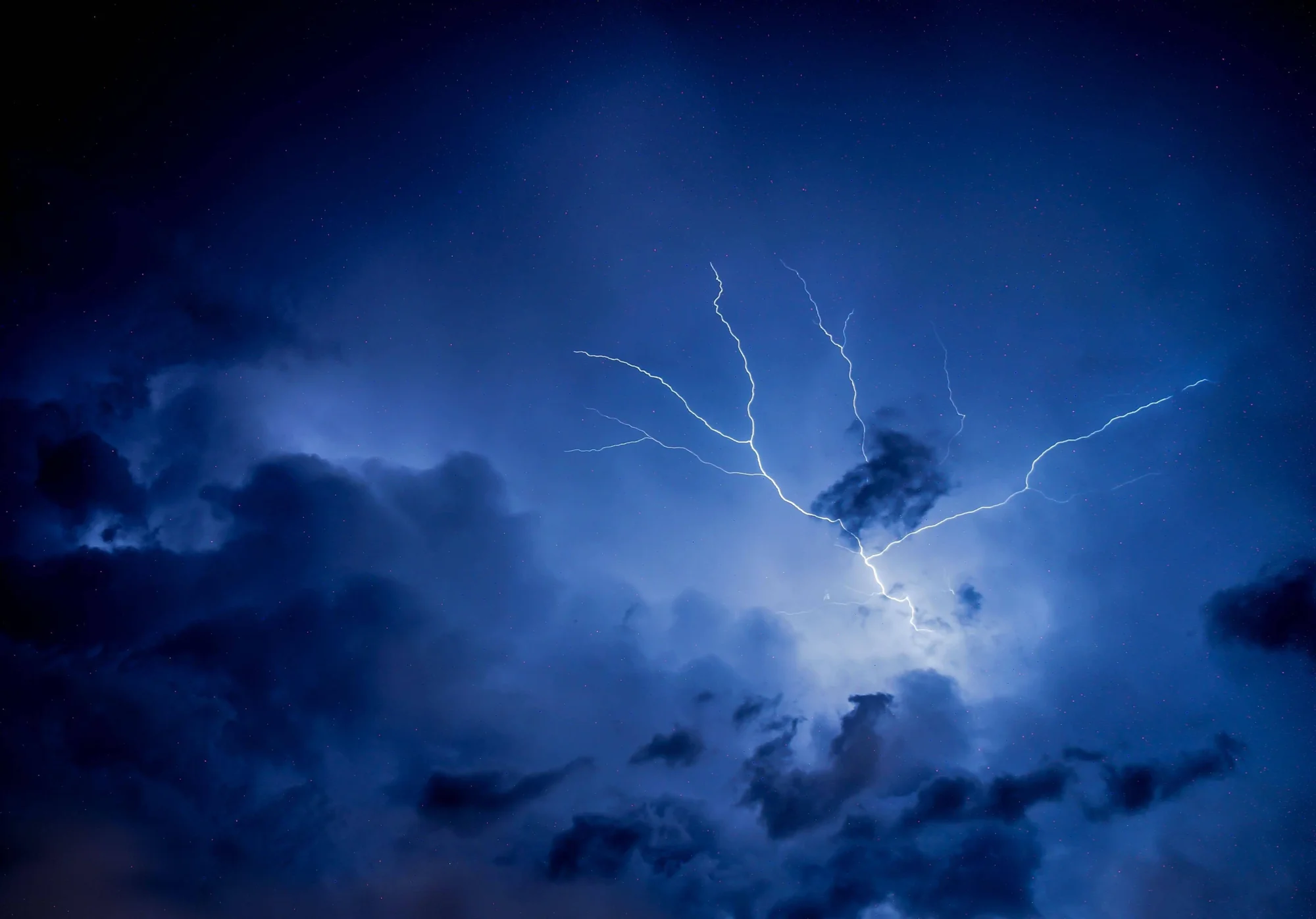 Rayo con múltiples ramificaciones ilumina nubes de tormenta en un cielo nocturno de tonos azules intensos.